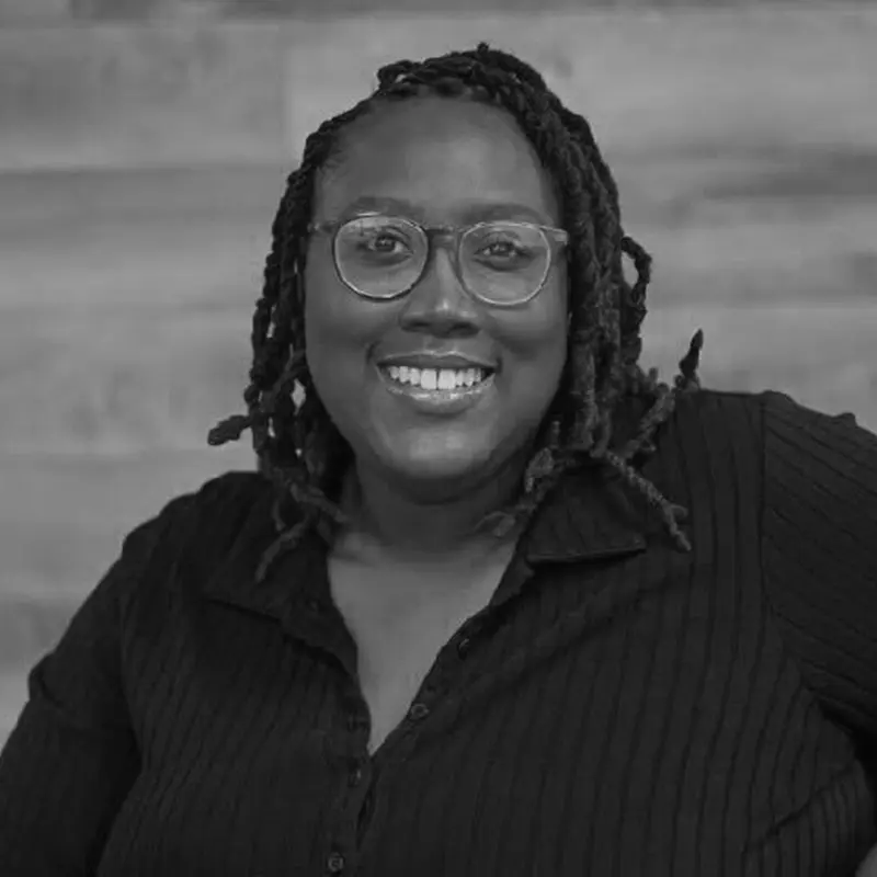 Black and white headshot of Lauren Neal smiling warmly, wearing glasses and a dark button-up shirt, against a softly textured background.